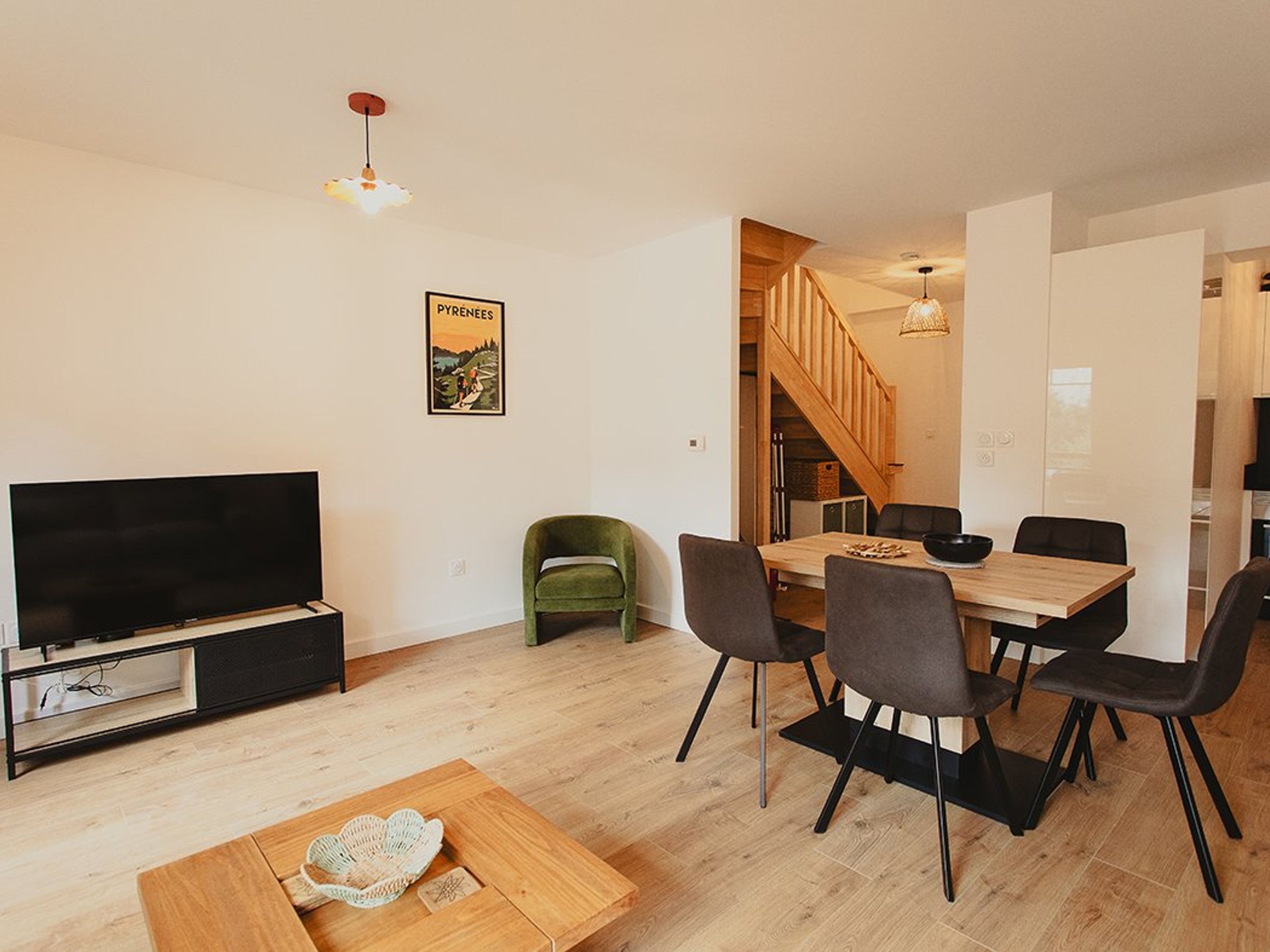 Een moderne woonkamer met een flatscreen televisie, een eethoek met een houten tafel en stoelen, en een trap naar een ander niveau.
