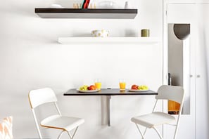 A modern kitchen with a white table, two white chairs, and a fruit plate with a glass of orange juice. - Parisian Studio Near Les Halles & Marais (Paris)