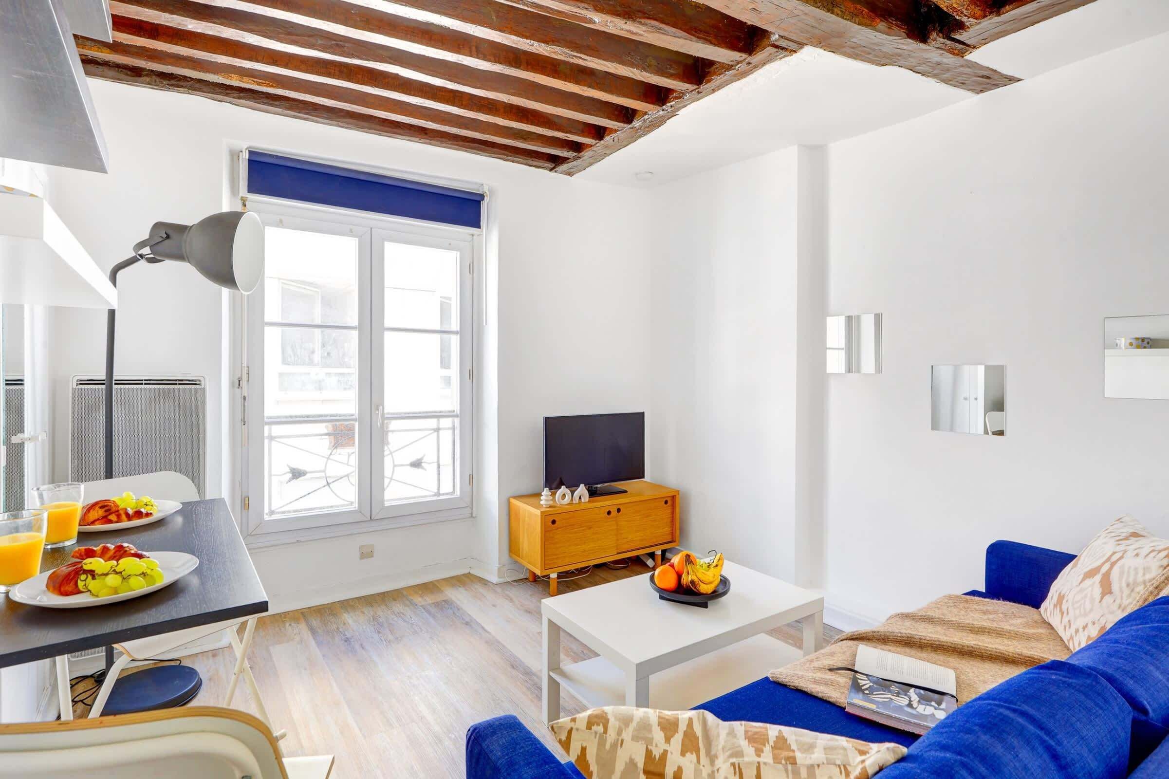 Una sala moderna con un sofá, una mesa de centro, un televisor y un comedor con una mesa y sillas.