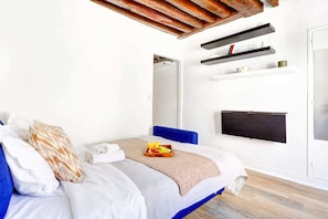 A modern bedroom with a bed, a TV mounted on the wall, and a small shelf with items. - Parisian Studio Near Les Halles & Marais (Paris)