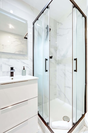 A modern bathroom with a glass-enclosed shower, a white vanity with a marble backsplash, and a large mirror above the sink. - Parisian Studio Near Les Halles & Marais (Paris)