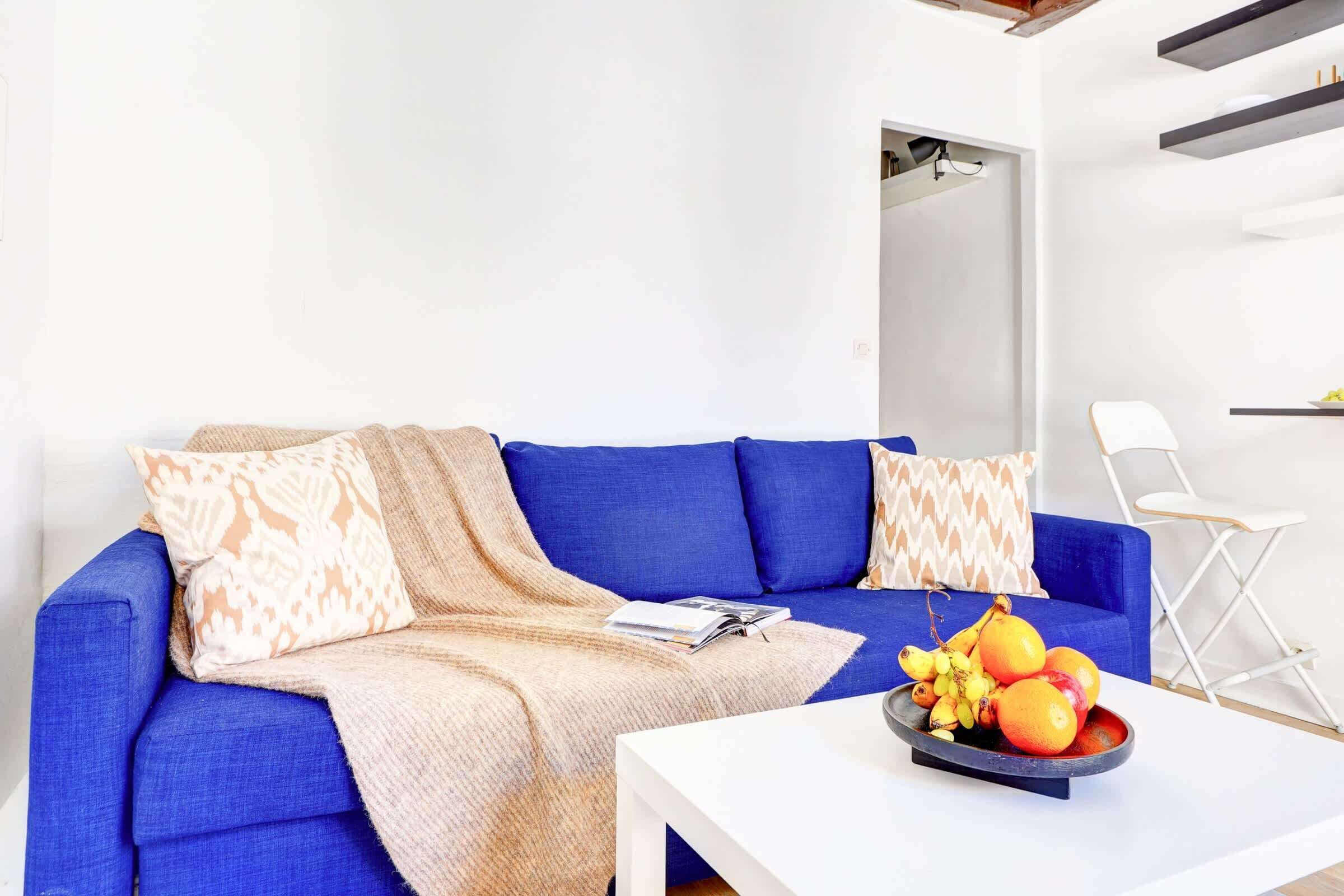 A modern living room with a blue sofa, a white coffee table, and a fruit bowl.