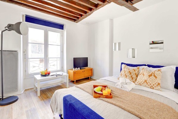 A modern bedroom with a bed, bedside table, TV, and a window with a view. - Parisian Studio Near Les Halles & Marais (Paris)