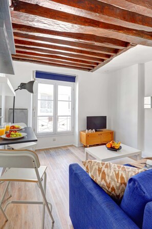 A modern living room with a blue sofa, a wooden coffee table, and a television. - Parisian Studio Near Les Halles & Marais (Paris)