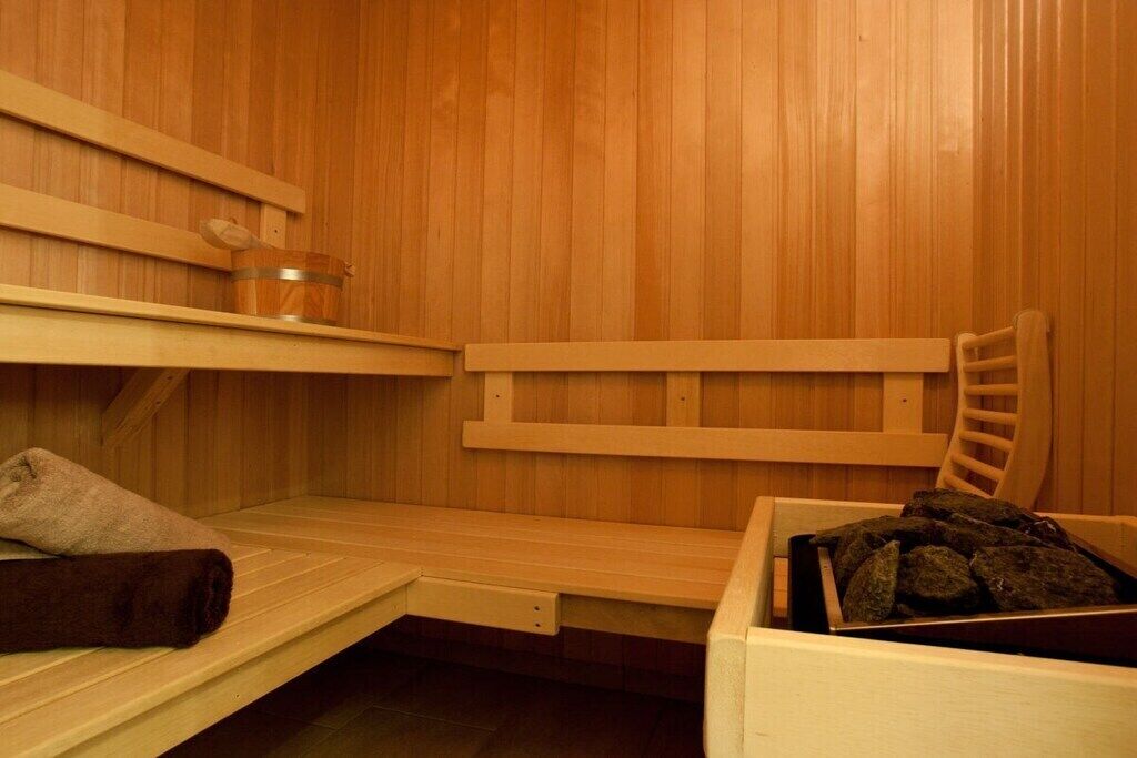 A sauna room with wooden benches, a bench with a towel, and a container with rocks.