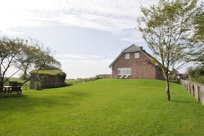 Een bakstenen huis met een schuin dak, een gazon en een houten omheining.