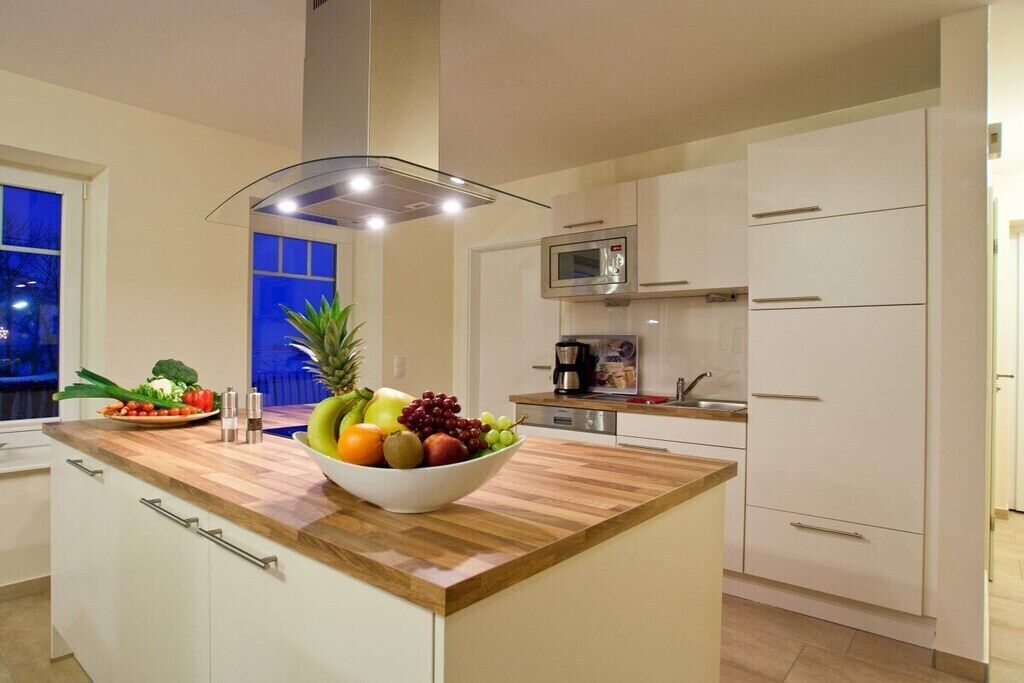 Een moderne keuken met een houten aanrecht, een fruitschaal, een magnetron en witte kastjes.