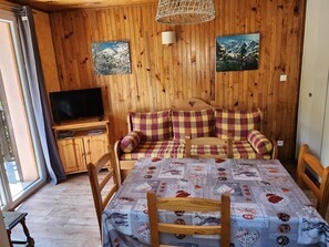 Ein gemütliches Zimmer mit Holzwänden, einem Fernseher, einem Sofa mit kariertem Bezug und einem Tisch mit gemustertem Tischläufer.