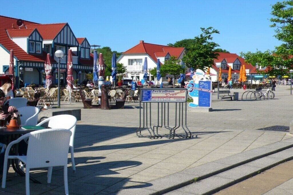 An outdoor seating area with tables and chairs, a signboard, and traditional buildings in the background.