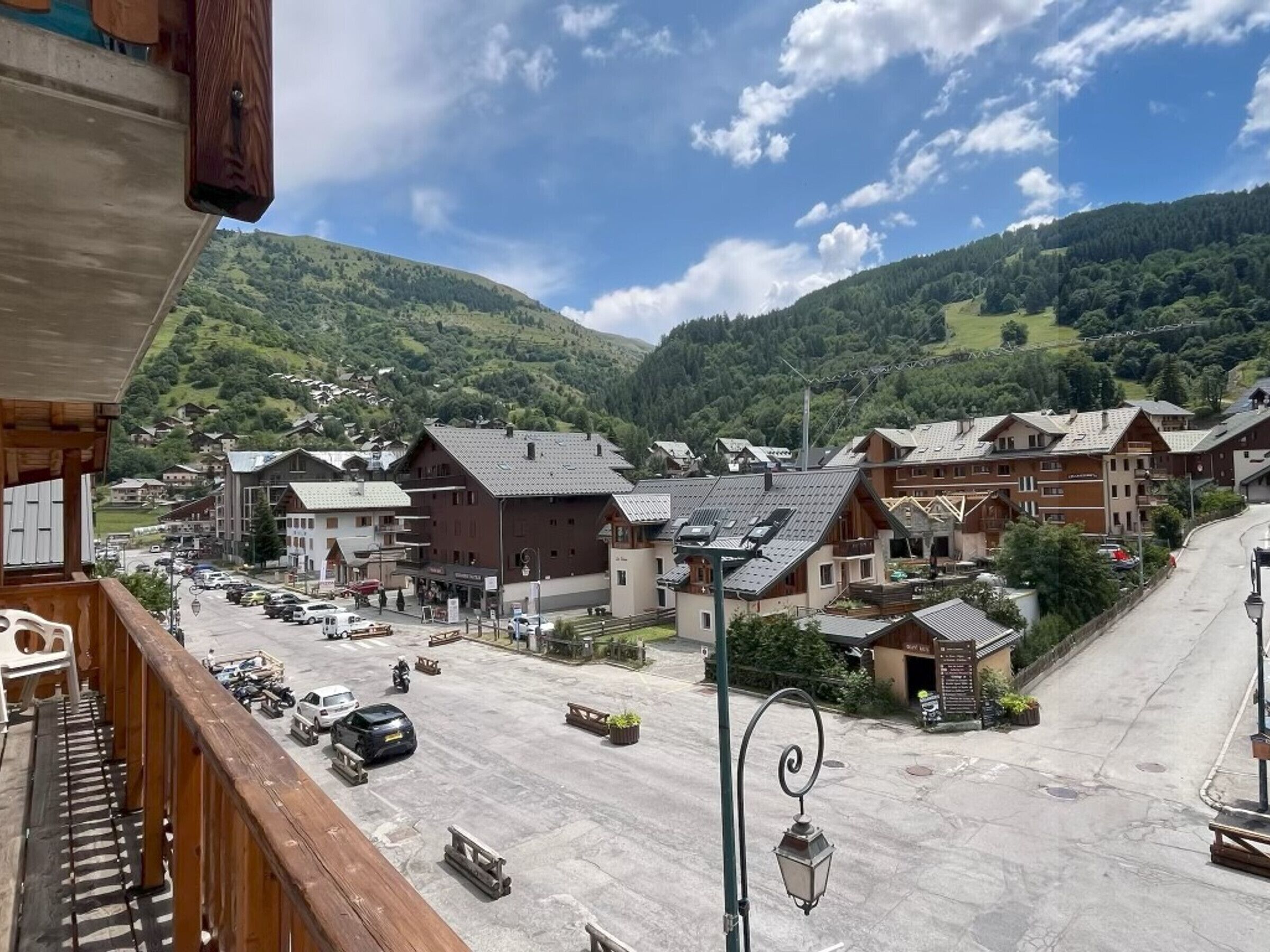 Une ville avec une place centrale, des bâtiments aux toits inclinés et une chaîne de montagnes en arrière-plan.