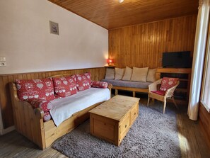 Ein gemütliches Zimmer mit einer Holzsofa, einem passenden Hocker, einem Fernseher und einem Korbstuhl.