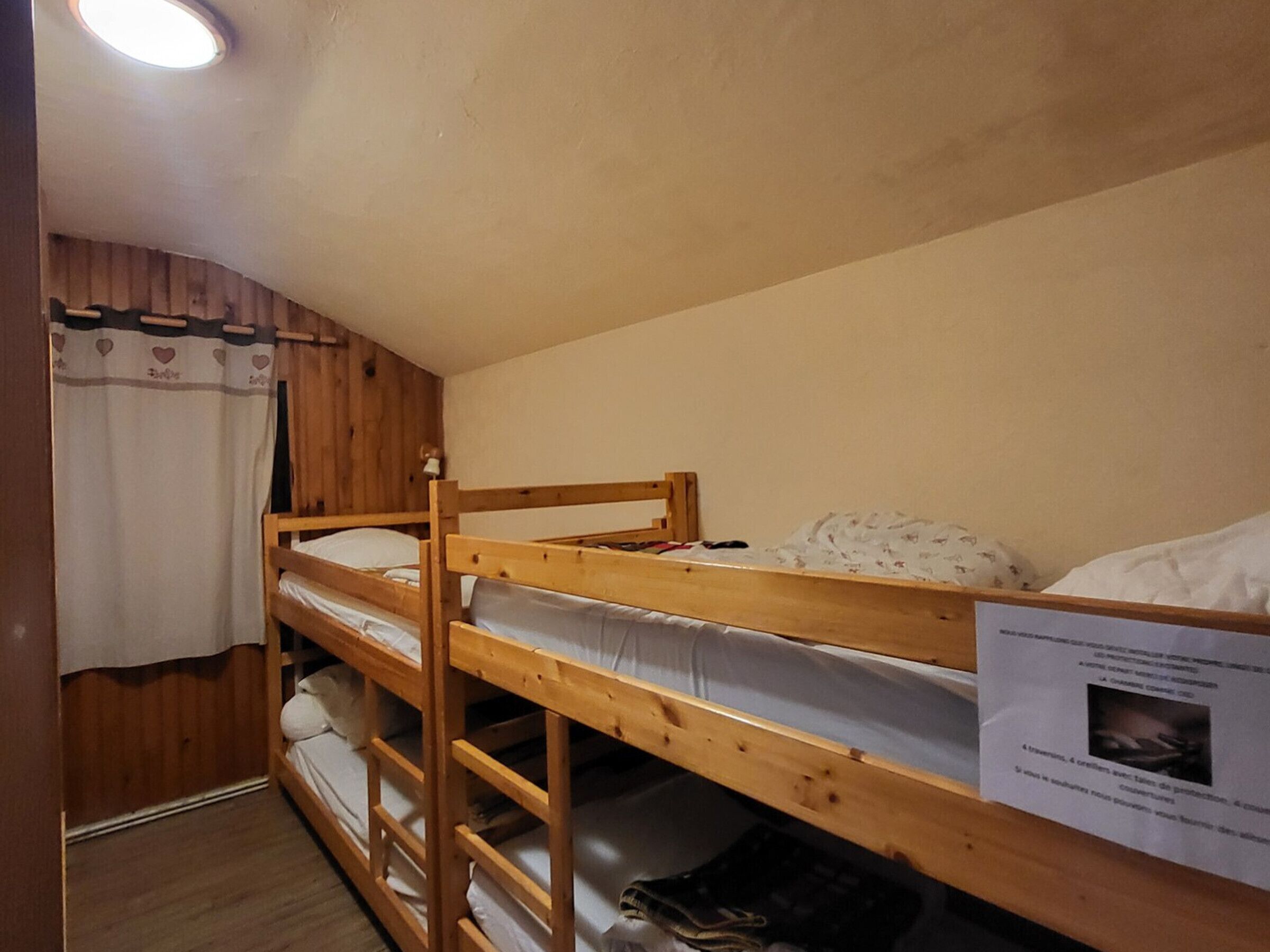 Een slaapkamer met een stapelbed, een houten hoofdbord, een gordijn en een bord aan de muur.