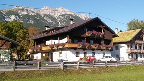 Een traditioneel chalet met een balkon, omringd door een houten hek en met een berg op de achtergrond.