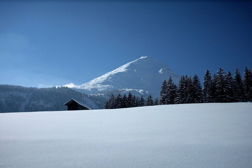 Een met sneeuw bedekte berg met een huisje op de voorgrond.