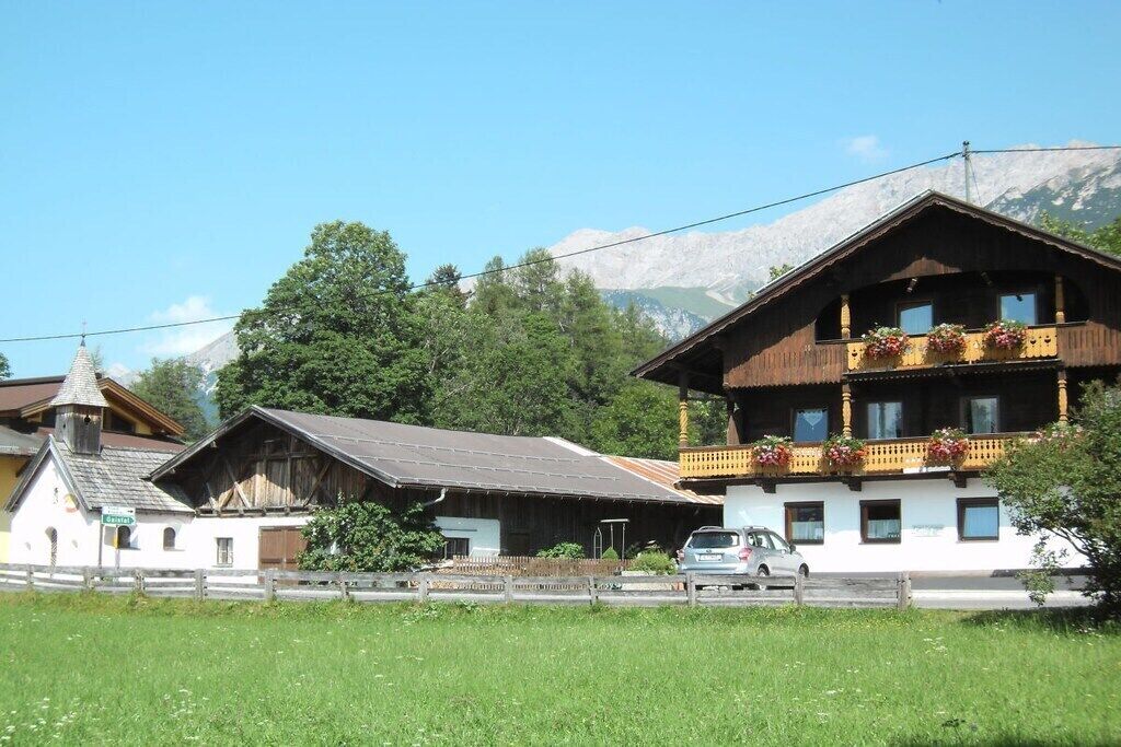 Ein traditionelles Holzhaus mit Balkon, ein Auto davor und ein Berg im Hintergrund.