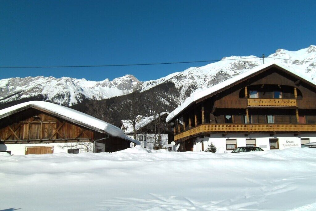 Een houten chalet met een balkon, met een besneeuwd berglandschap op de achtergrond.