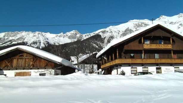 Een houten chalet met een balkon, met een besneeuwd berglandschap op de achtergrond.