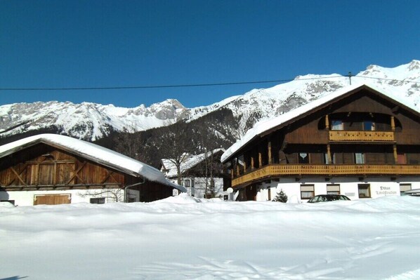 A wooden chalet with a balcony, set against a backdrop of snow-covered mountains. - in the Landfrieden House (Leutasch)