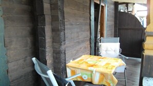Een houten gevel met een overdekte veranda, een tafel met een bloemrijk tafelkleed en een stoel.