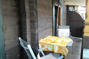 A wooden exterior with a covered porch, a table with a floral tablecloth, and a chair. - in the Landfrieden House (Leutasch)