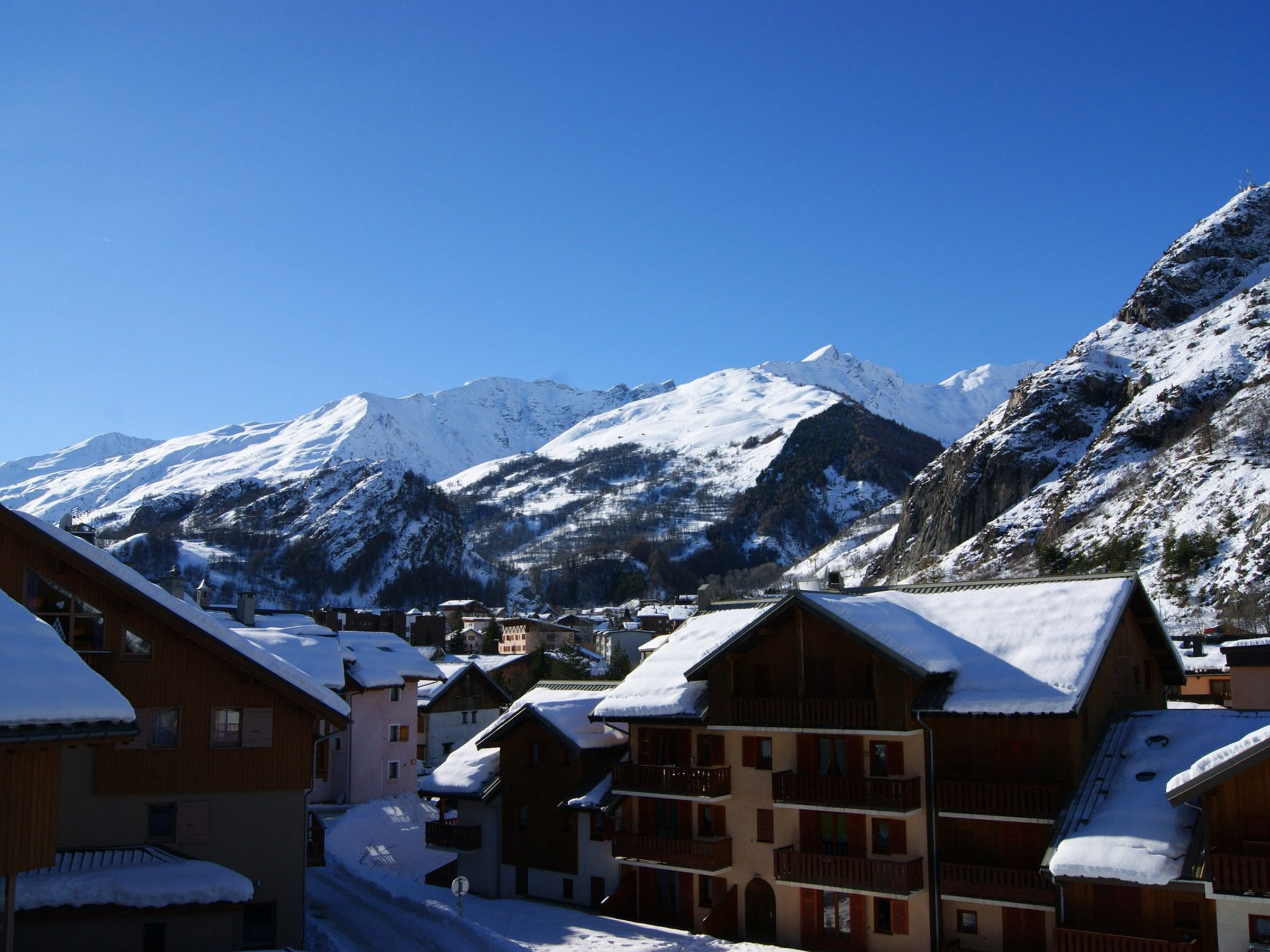 A snow-covered mountain village with wooden buildings and a clear blue sky.
