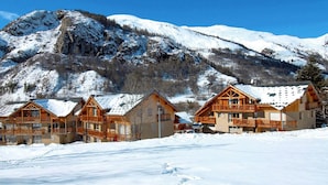 A row of wooden cabins with balconies, set against a backdrop of snow-covered mountains and clear blue sky. - Spacious apartment - 6 guests (Valloire)