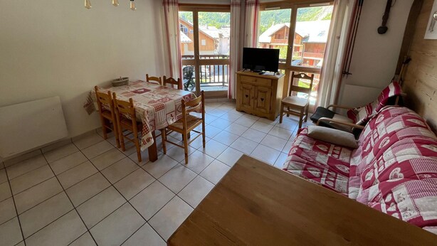 A room with a dining table, chairs, a sofa, a television, and a balcony with curtains. - Spacious apartment - 6 guests (Valloire)