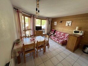 Ein gemütliches Zimmer mit Esstisch, Stühlen, einer Couch, einem Fernseher und einer Mikrowelle.