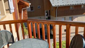 A balcony with a glass table and two chairs, wooden railings, and a view of neighboring buildings. - Spacious apartment - 6 guests (Valloire)