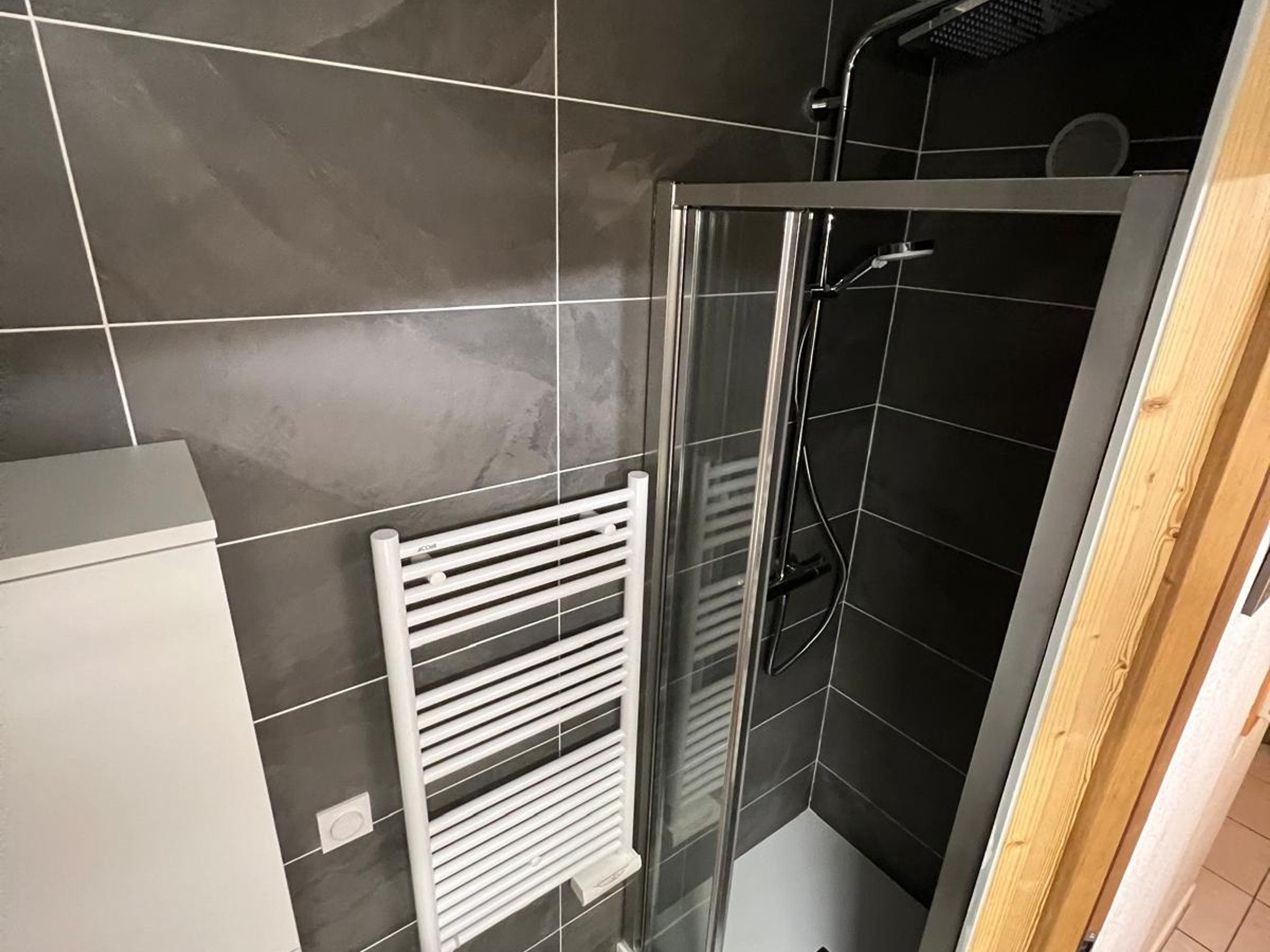 Ein modernes Badezimmer mit einer Duschkabine aus Glas, einem weißen Handtuchhalter und dunkel gefliesten Wänden.