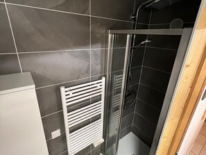Ein modernes Badezimmer mit einer Duschkabine aus Glas, einem weißen Handtuchhalter und dunkel gefliesten Wänden.