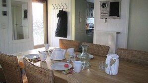 Zona pranzo con tavolo in legno, sedie in vimini e una cucina sullo sfondo.