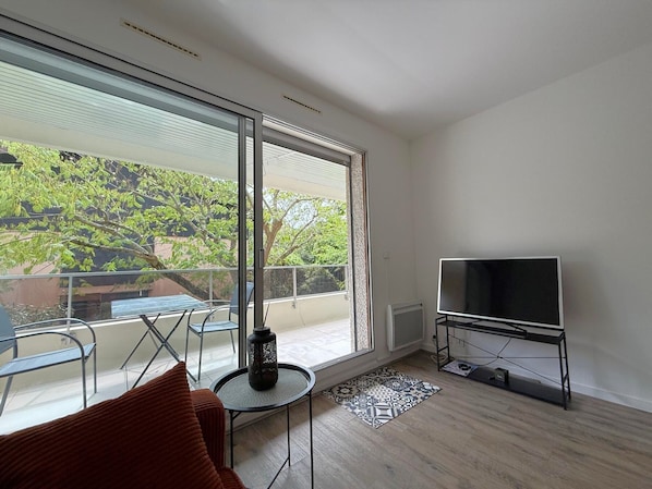 Ein modernes Wohnzimmer mit großem Fenster, Flachbildfernseher und kleinem runden Tisch.