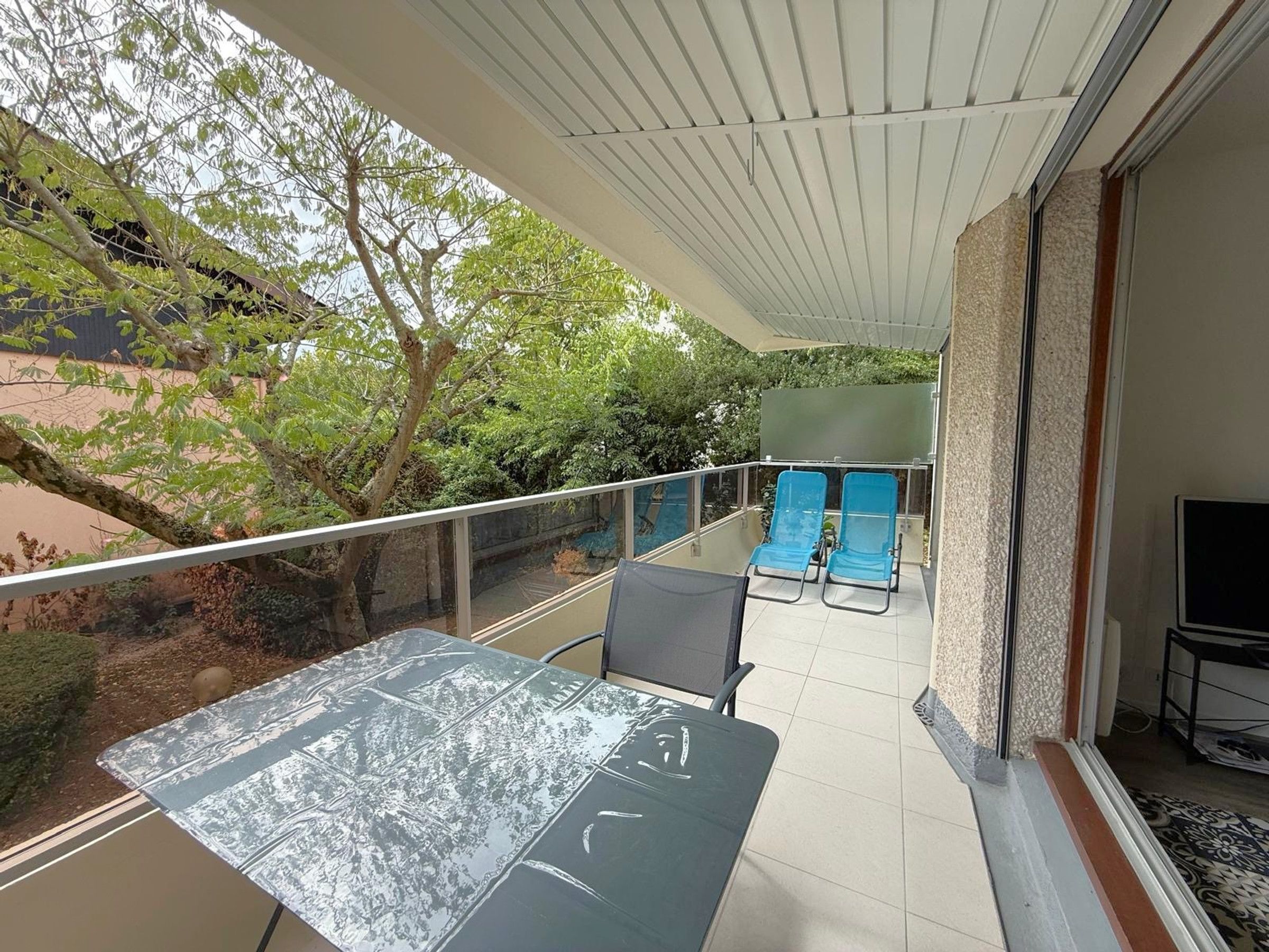 A balcony with a table and chairs, a TV, and a view of trees and a building.
