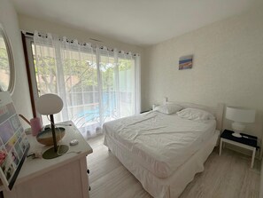 Ein Schlafzimmer mit einem Bett, einem Nachttisch mit Lampe, einem Schreibtisch mit Spiegel und einem Fenster mit Vorhängen.
