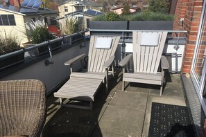 Eine Dachterrasse mit zwei Adirondack-Stühlen, einem kleinen Tisch und einem Korbstuhl.