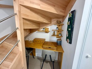Ein kompakter Raum mit Schreibtisch aus Holz, einem Stuhl, einer kleinen Ablage mit Dekoration und einer Treppe.