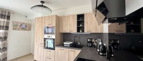 Eine moderne Küche mit Holzschränken, einem eingebauten Backofen, einer Kaffeemaschine und einer schwarzen Arbeitsplatte.