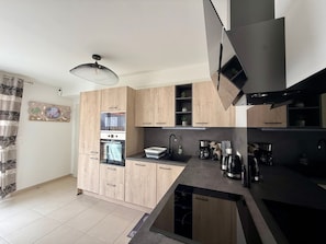 A modern kitchen with wooden cabinets, a built-in oven, a coffee maker, and a black countertop. - Modern house near forest - PMR - 6 guests (Saint-Jean-de-Monts)