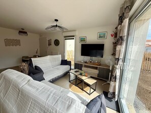 A living room with a sofa, a coffee table, a TV, and a fan. - Modern house near forest - PMR - 6 guests (Saint-Jean-de-Monts)