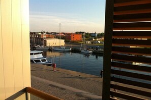A harbor with boats docked, a building in the background, and a view through a window with blinds. - Sharp "Utkiek" || Wismar (Wismar)