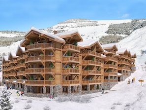 Eine mehrstöckige Holzhütte mit Balkonen vor einer verschneiten Berglandschaft.