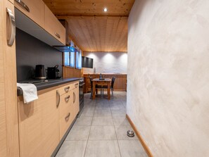 A compact kitchen with wooden cabinets, a coffee maker, a dining table with chairs, and a flat-screen TV mounted on the wall. - Cozy apartment with Wi-Fi - 2 guests (Les Gets)