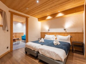 Een slaapkamer met een houten plafond, een bed met witte lakens, een bankje en een kleine tafel.