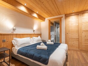 A wooden-paneled bedroom with a bed, bedside tables, and a walk-in closet. - Cozy apartment with Wi-Fi - 2 guests (Les Gets)