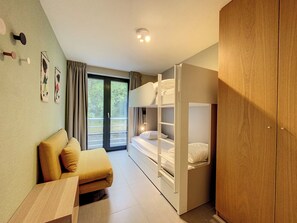 Una habitación con sofá, cama con cabecera, armario y puerta corredera de vidrio que da a un espacio exterior.