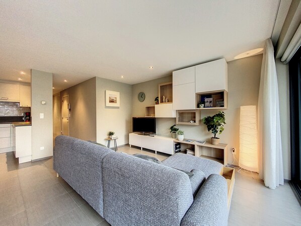 Una sala de estar moderna con un sofá gris, un televisor de pantalla plana y estanterías empotradas con objetos decorativos.