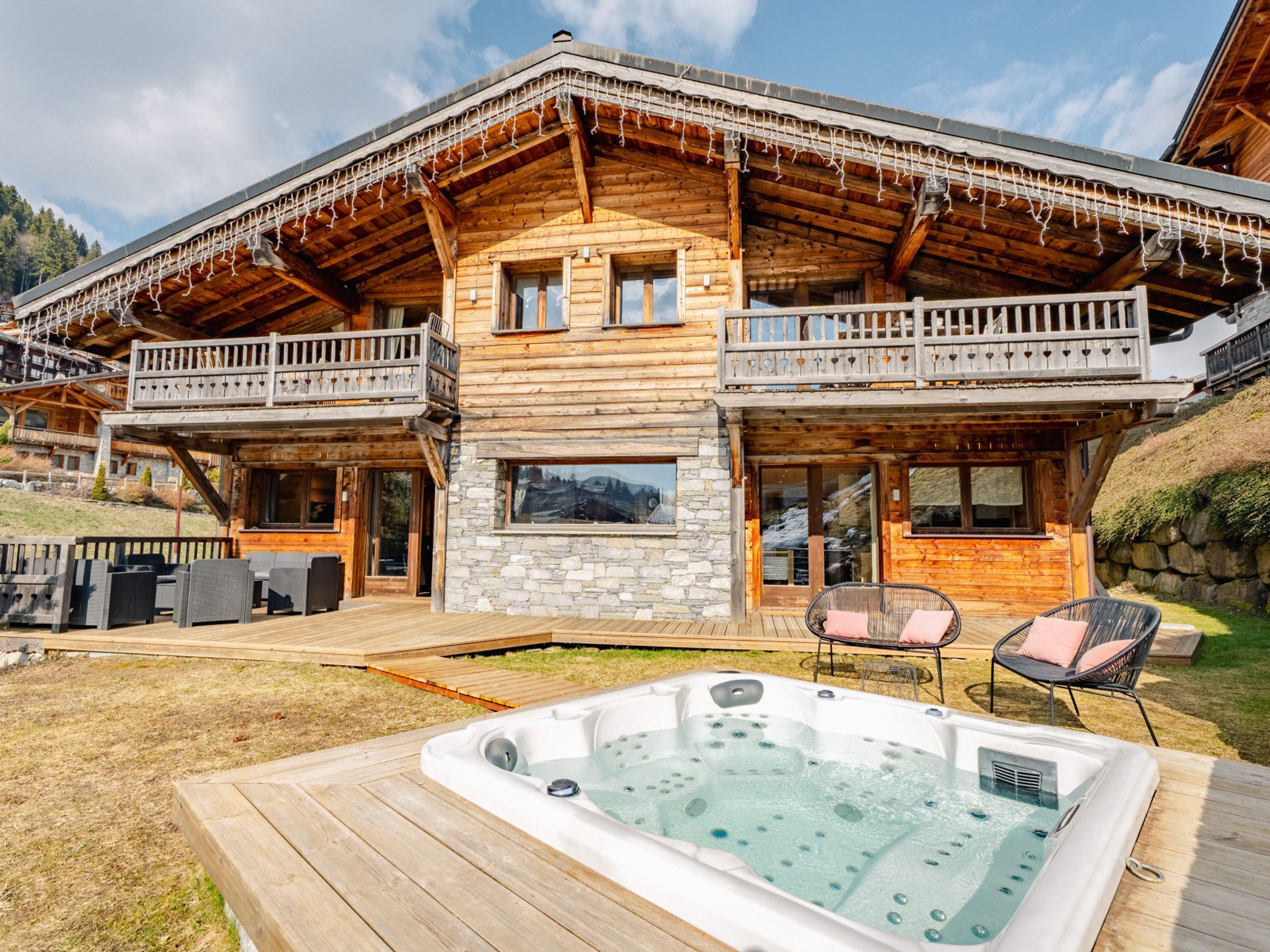 Un chalet en bois doté d’un bain à remous, d’un espace extérieur aménagé et d’une fa çade en pierre.
