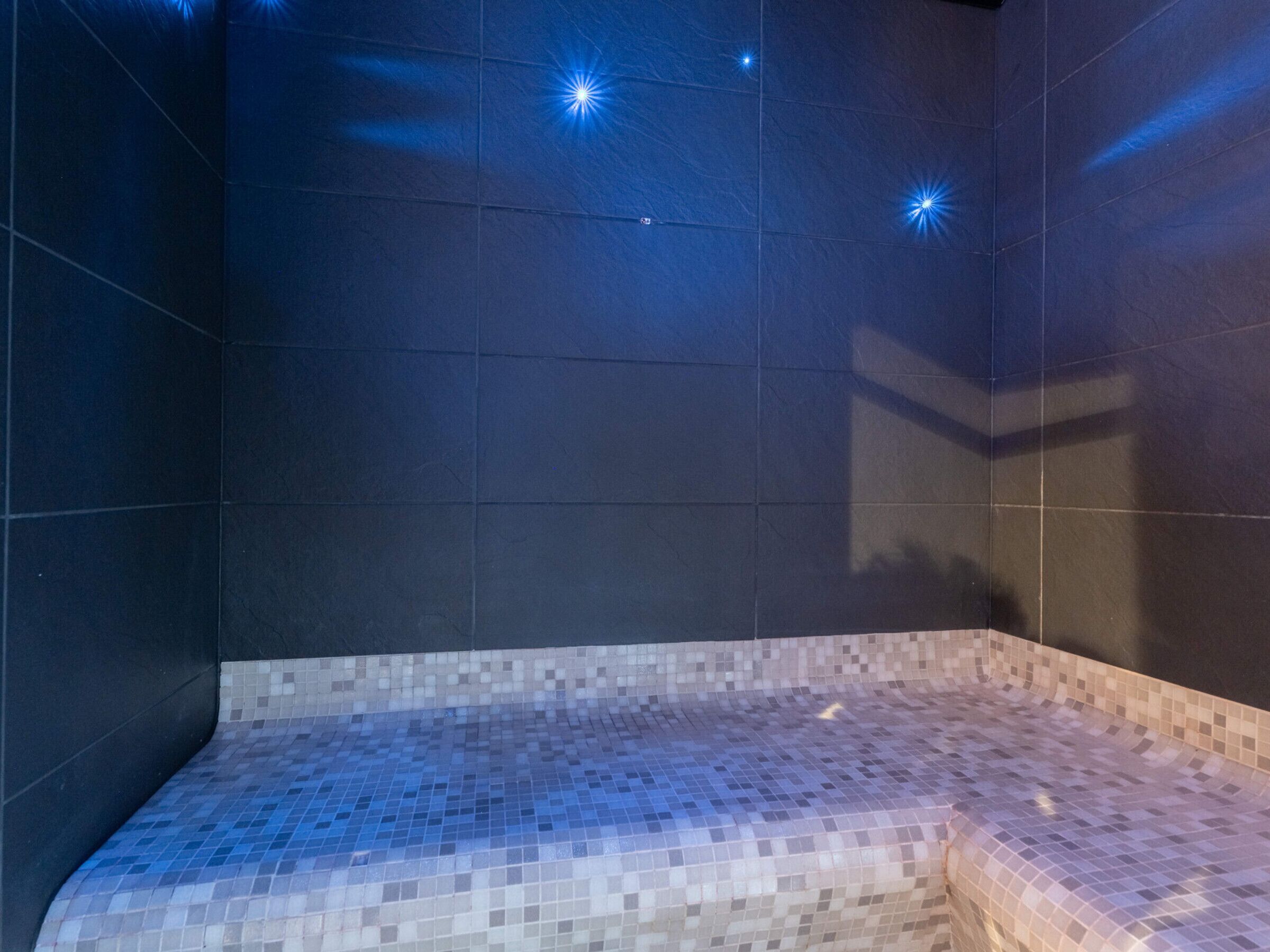 A tiled room with a curved bench and a wall-mounted light fixture.