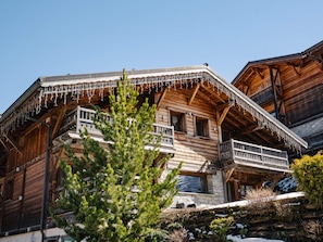 A wooden chalet with balconies, stone walls, and a pine tree in the foreground. - Spacious apartment, jacuzzi, parking - 15 guests (Les Gets)
